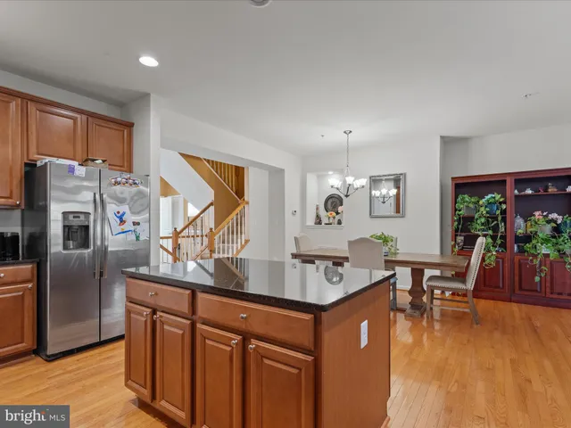 a living room with stainless steel appliances granite countertop a refrigerator a sink dishwasher a dining table and chairs with wooden floor