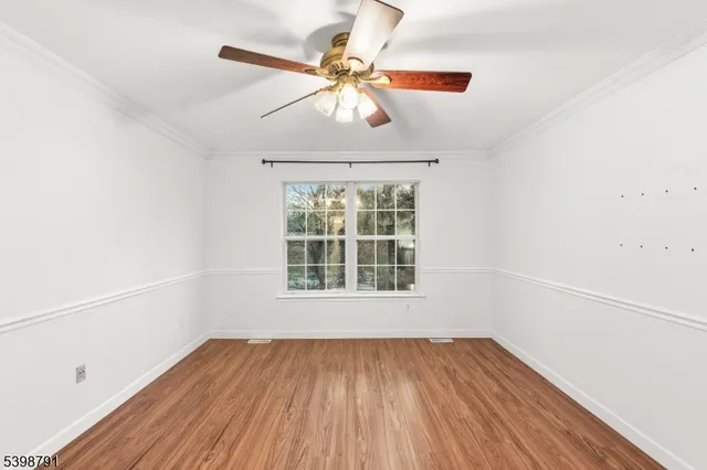 an empty room with wooden floor chandelier fan and windows