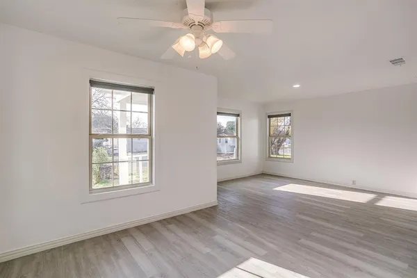 an empty room with wooden floor chandelier fan and windows