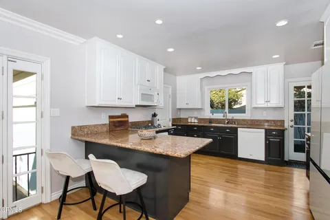 a kitchen with a stove a sink a kitchen island with chairs and wooden floor