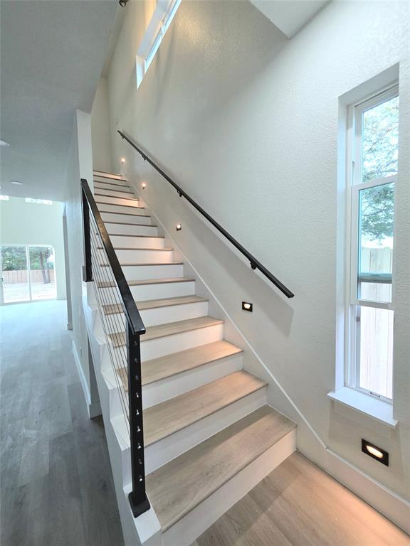 3905 Blue Ridge Boulevard Dallas, TX 75233 - Photo 7 of 9 Modern staircase featuring wood-finish treads, white risers, and a contemporary metal railing with horizontal balusters