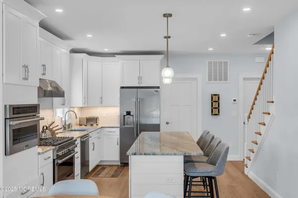 a kitchen with stainless steel appliances kitchen island granite countertop a sink a stove a refrigerator cabinets and chairs