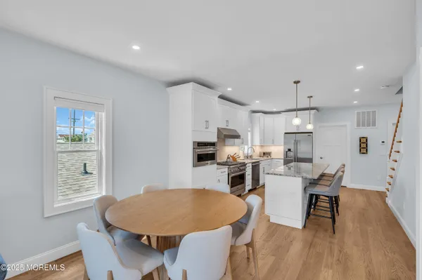 a living room with stainless steel appliances a dining table wooden floor and a kitchen view