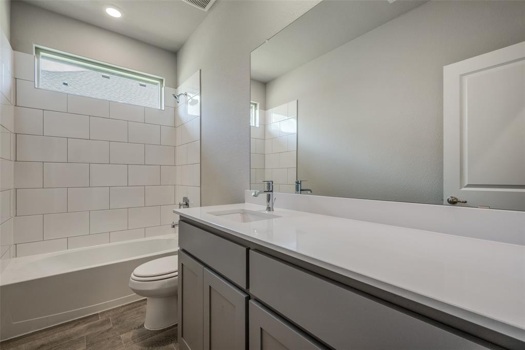 5231 Meadow Lane Krum, TX 76249 - Photo 10 of 17 Bathroom featuring a modern vanity with a white countertop and integrated sink, a large wall-mounted mirror, a white subway tile tub surround, a white bathtub, and wood-finish flooring