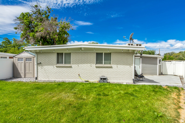 48 Moon Ridge Drive Murray, UT 84107 - Photo 22 of 30 Rear exterior featuring light-colored brick siding, a concrete patio, a detached storage shed, a white privacy fence, and a manicured lawn
