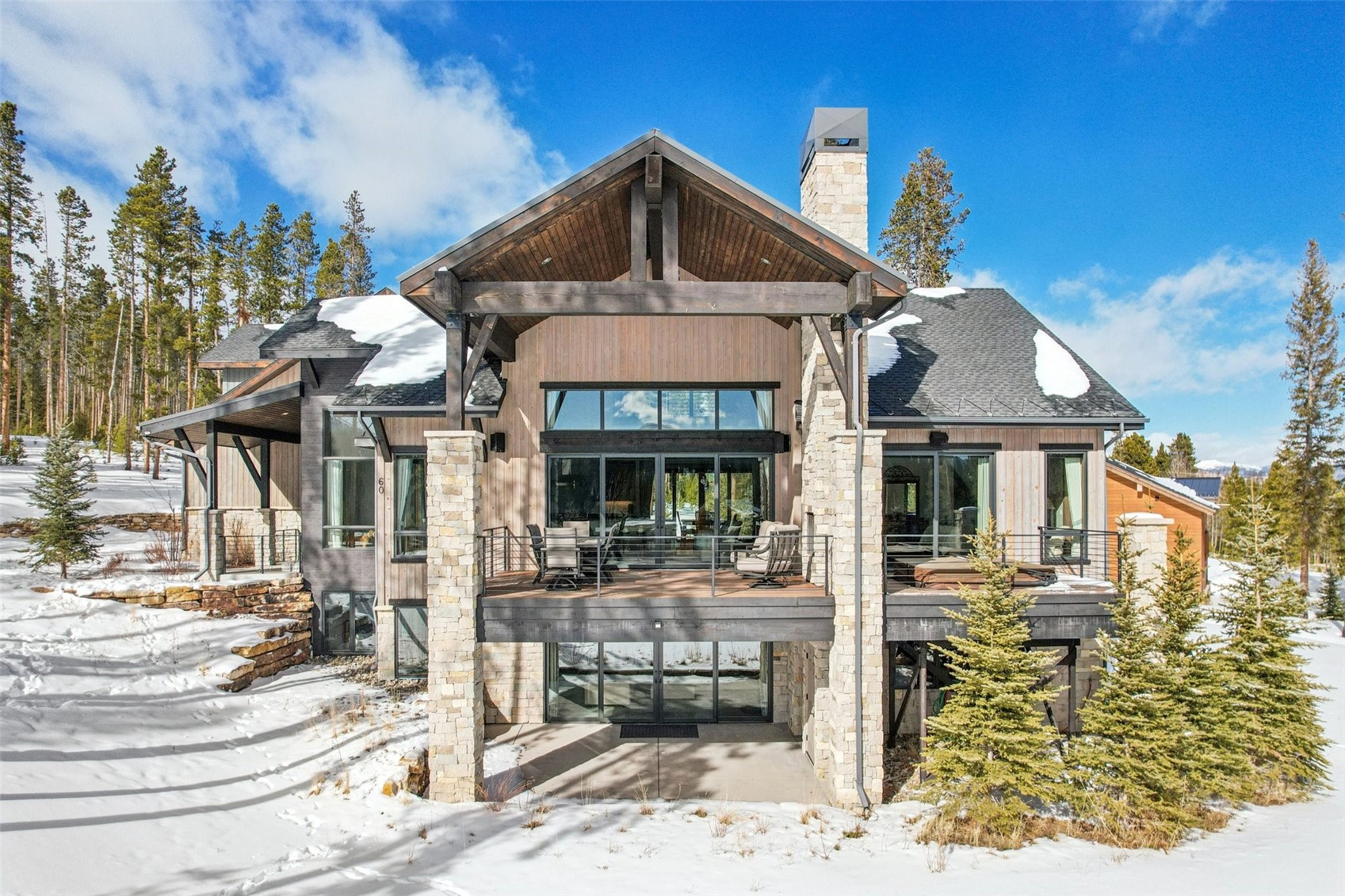 Snow covered house featuring roof with shingles, a patio, stone siding, and a chimney