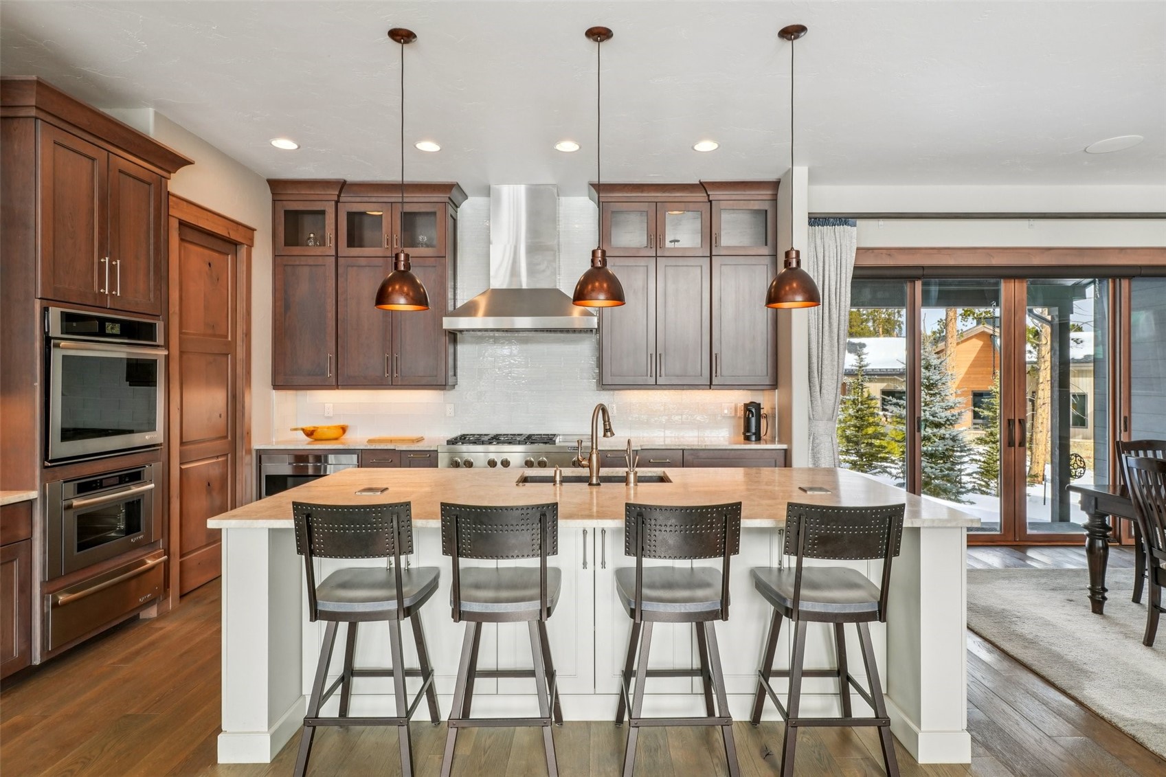 60 Barton Ridge Drive Breckenridge, CO 80424 - Photo 16 of 50 Kitchen with hanging light fixtures, a kitchen island with sink, a breakfast bar, dark wood-type flooring, and glass fronted cabinets