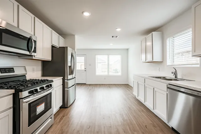 a kitchen with stainless steel appliances a stove a sink cabinets and a wooden floor