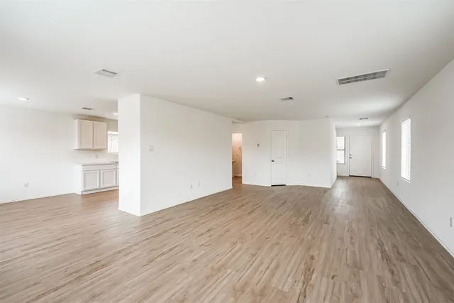 a view of empty room with wooden floor and kitchen