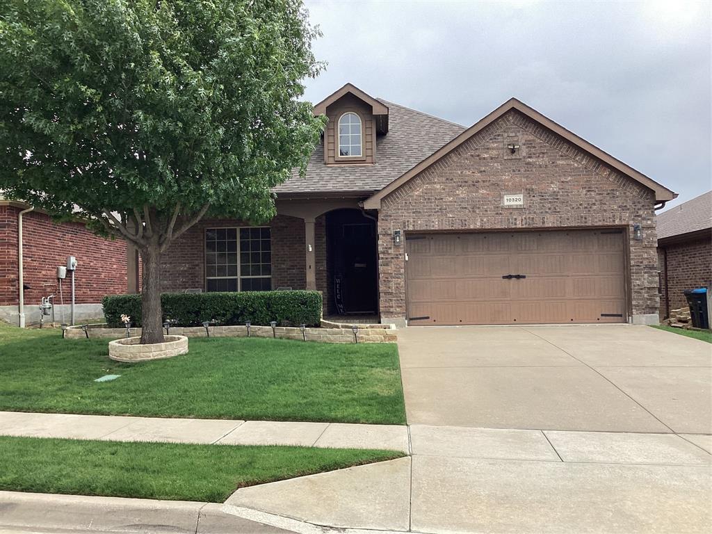 Brick facade residence featuring a two-car garage, manicured lawn with mature tree, and concrete driveway