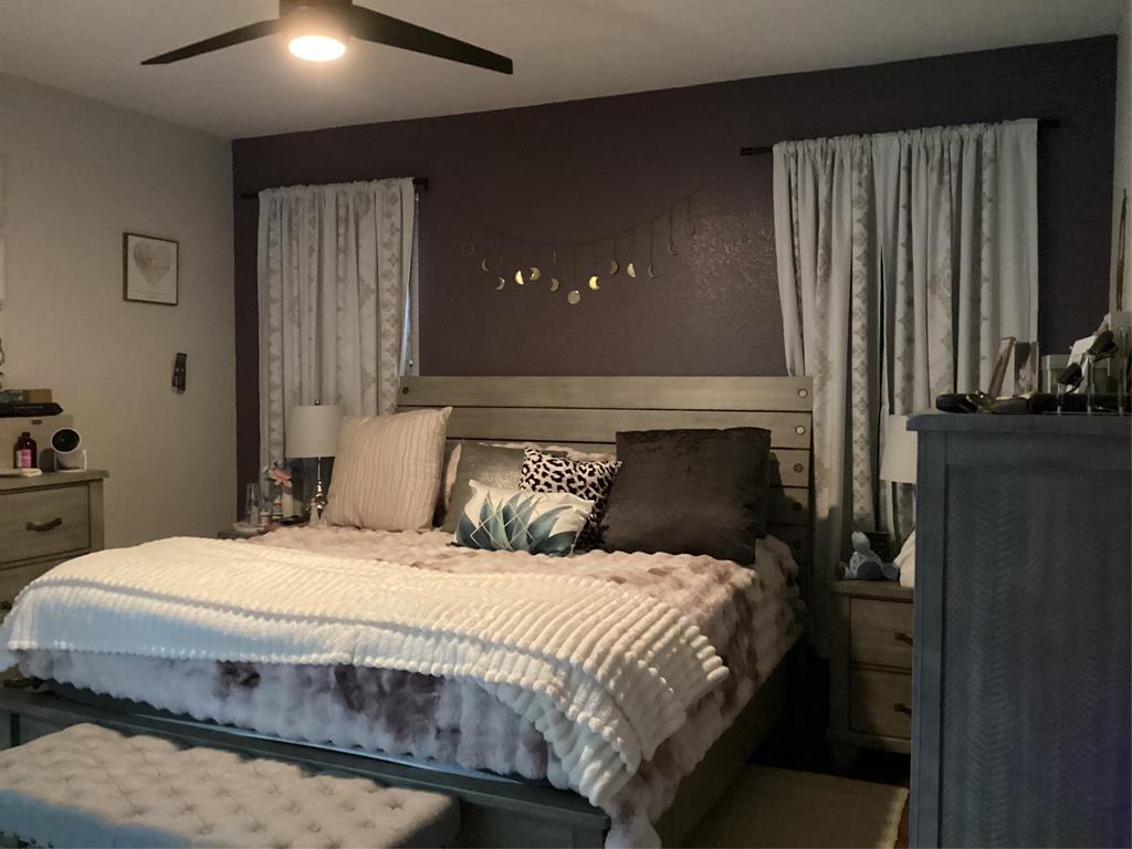 10320 Point Lobos Trail Fort Worth, TX 76177 - Photo 13 of 33 Bedroom featuring a dark accent wall, a ceiling fan with integrated lighting, and light-toned window treatments