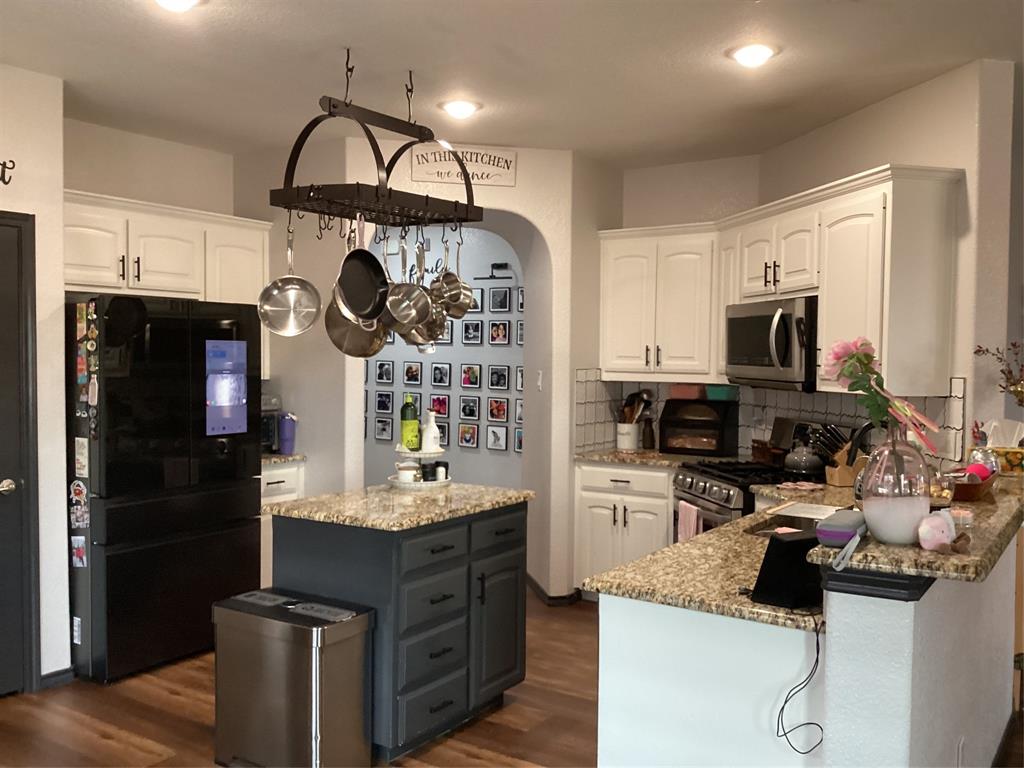 10320 Point Lobos Trail Fort Worth, TX 76177 - Photo 5 of 33 Kitchen featuring wood-finish flooring, a central island with dark cabinetry and a granite-style countertop, white perimeter cabinetry with a matching granite-style countertop, and a stainless steel oven/range and microwave