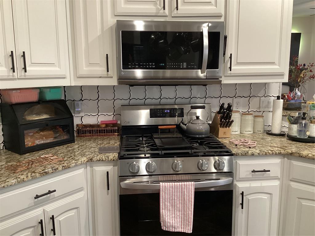 10320 Point Lobos Trail Fort Worth, TX 76177 - Photo 7 of 33 Kitchen featuring a stainless steel gas range and microwave, white shaker-style cabinetry with dark hardware, a tile backsplash with a Moroccan quatrefoil pattern, and speckled granite countertops