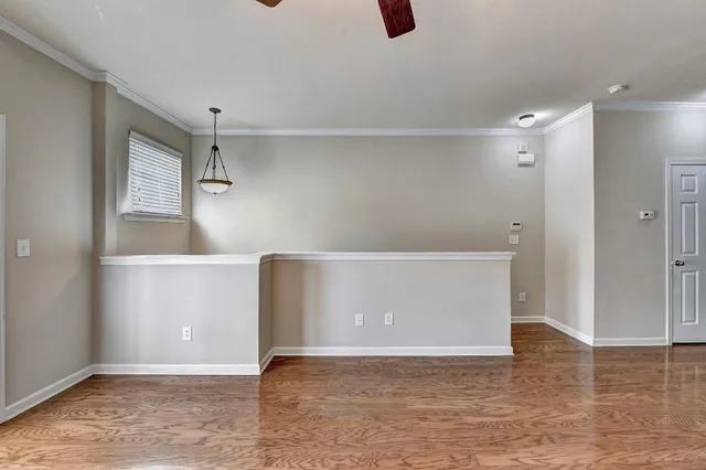 a view of an empty room with wooden floor and a ceiling fan