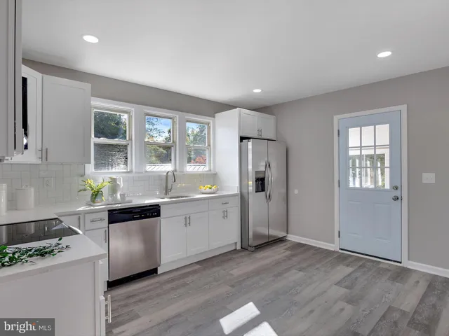 a kitchen with stainless steel appliances granite countertop a refrigerator a sink a stove and white cabinets with wooden floor