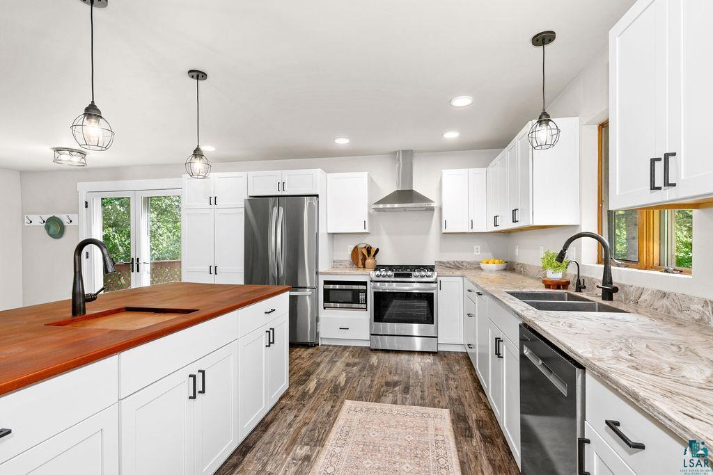 5025 Reid Road Duluth, MN 55803 - Photo 12 of 51 Modern kitchen featuring white shaker cabinetry, stainless steel appliances, wood-finish flooring, a large island with an integrated sink, and dual pendant lighting fixtures