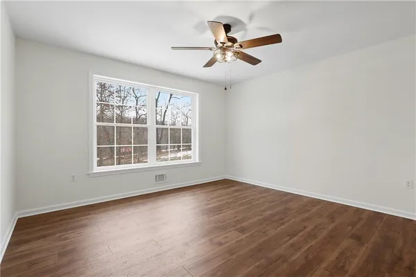 an empty room with wooden floor fan and windows