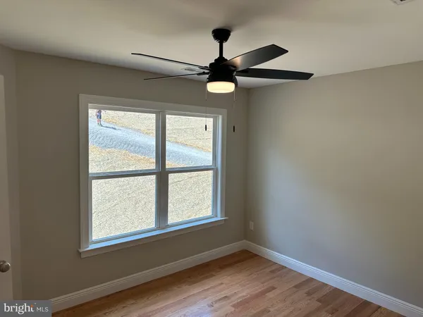an empty room with wooden floor fan and windows
