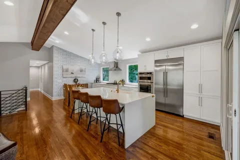 a kitchen with stainless steel appliances kitchen island granite countertop a kitchen island a stove a refrigerator a sink a dining table and chairs with wooden floor