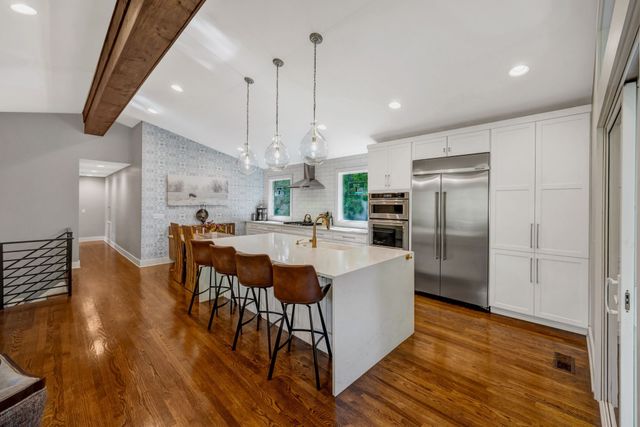 a kitchen with stainless steel appliances kitchen island granite countertop a kitchen island a stove a refrigerator a sink a dining table and chairs with wooden floor