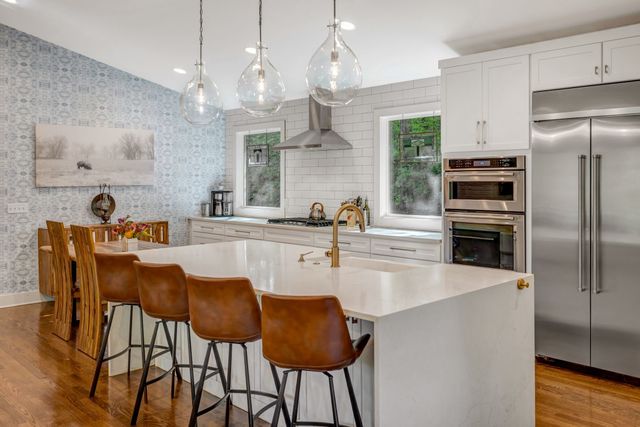 a kitchen with stainless steel appliances granite countertop a refrigerator a sink dishwasher a dining table and chairs with wooden floor