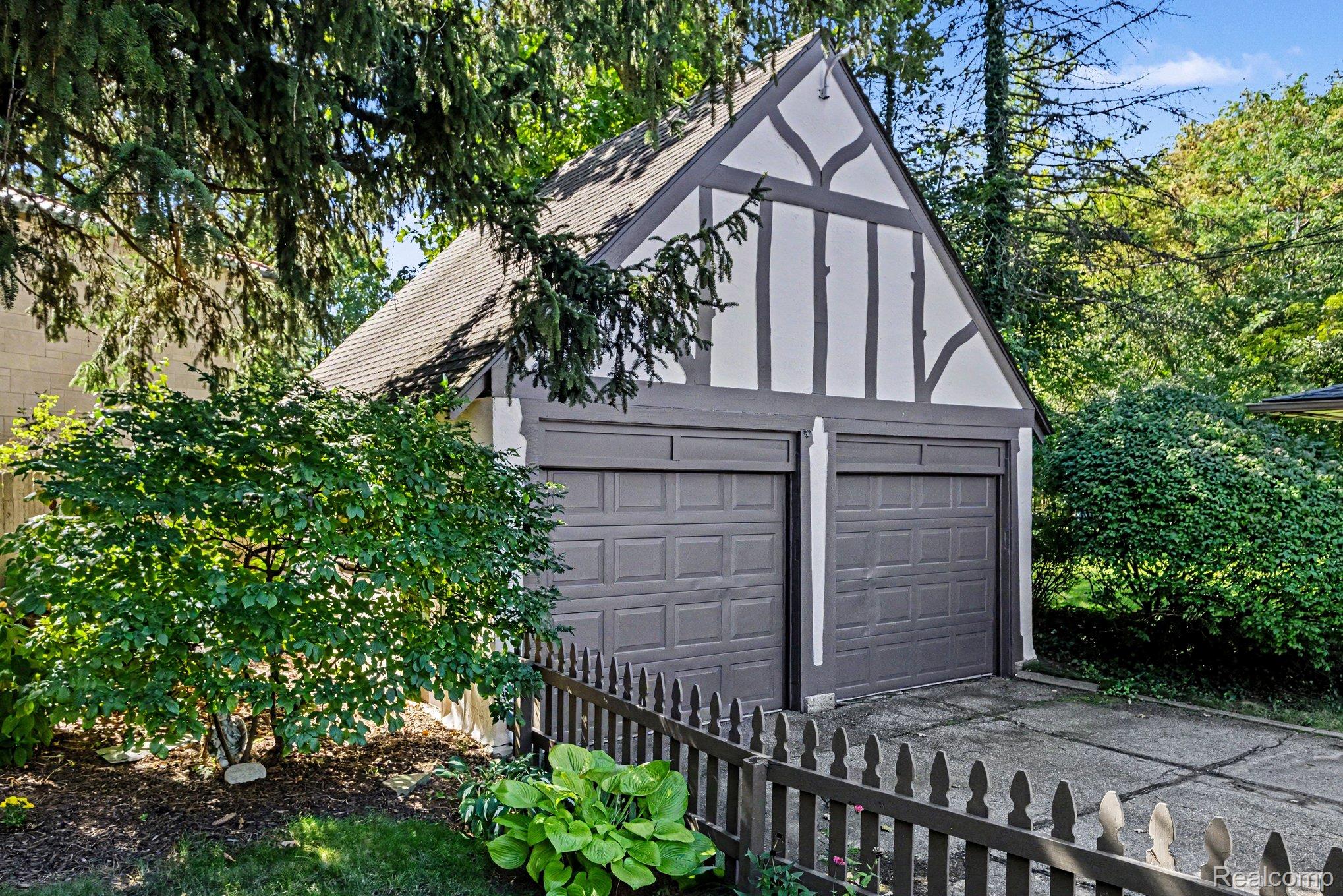 2030 Hampden Road Flint, MI 48503 - Photo 31 of 34 Tudor-style detached garage with two garage doors, featuring a white and dark trim facade, a dark shingle roof, and a dark picket fence