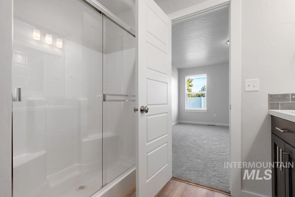1340 Dawn Street Weiser, ID 83672 - Photo 18 of 32 Bathroom with vanity, light wood-style flooring, a shower stall, light carpet, and a textured ceiling