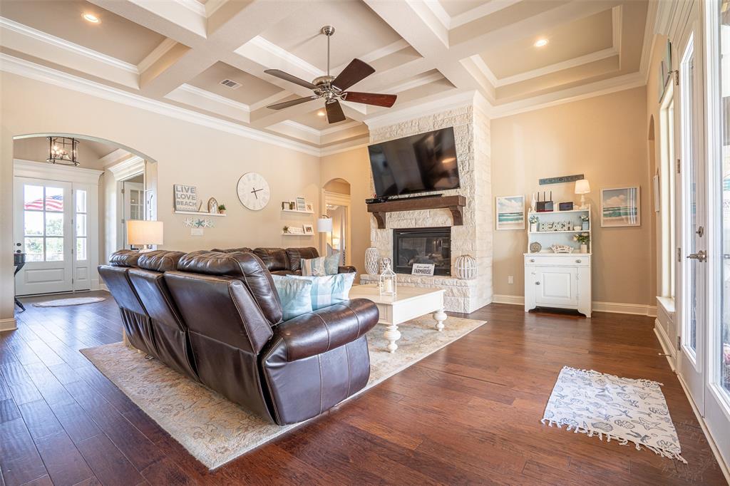 1920 Meander Road Granbury, TX 76049 - Photo 9 of 40 Living area featuring wood-finish flooring, a stone fireplace with a wood mantle, and a coffered ceiling with a ceiling fan
