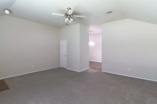 an empty room with a chandelier fan and kitchen view