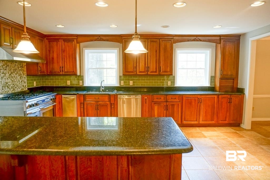 255 Suffolk Road Mobile, AL 36608 - Photo 10 of 29 Kitchen with dark stone counters, stainless steel appliances, hanging light fixtures, light tile patterned flooring, and wood finish cabinets