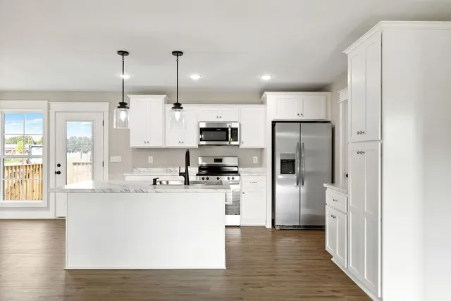 a kitchen with stainless steel appliances granite countertop a refrigerator a sink dishwasher a stove oven and white countertops with wooden floor