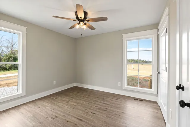 an empty room with wooden floor fan and windows