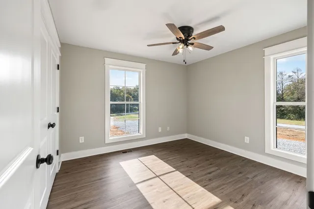 an empty room with wooden floor fan and windows