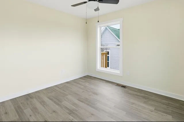 an empty room with wooden floor fan and windows