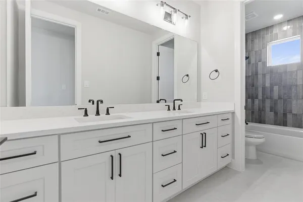 a spacious bathroom with double sink a toilet a shower and a mirror