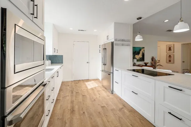 a large white kitchen with a refrigerator a sink and cabinets