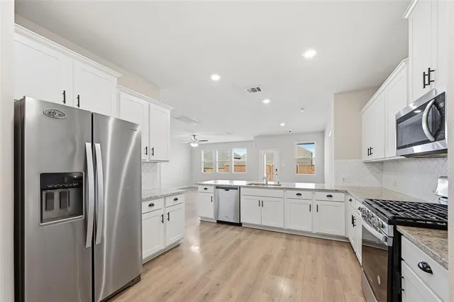 a kitchen with stainless steel appliances granite countertop a refrigerator a sink dishwasher a stove and white cabinets with wooden floor