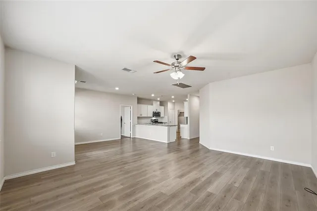 a view of an empty room and kitchen view with wooden floor