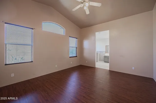 an empty room with wooden floor chandelier fan and windows