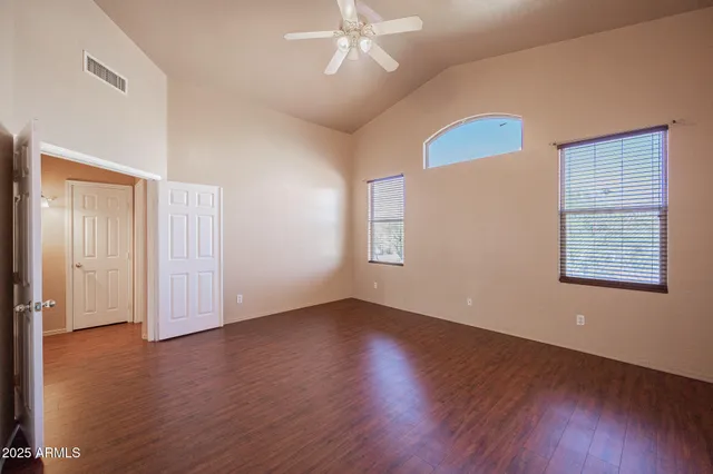 an empty room with wooden floor chandelier fan and windows
