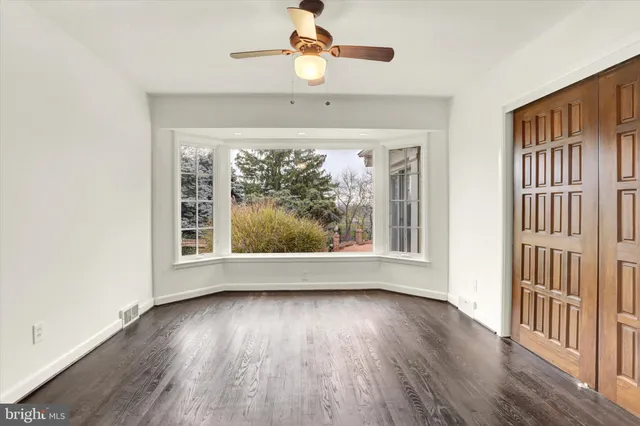 an empty room with wooden floor fan and windows