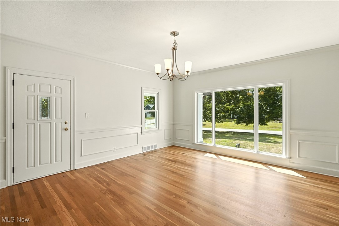 Unfurnished dining area featuring a decorative wall, a chandelier, wood finished floors, ornamental molding, and wainscoting