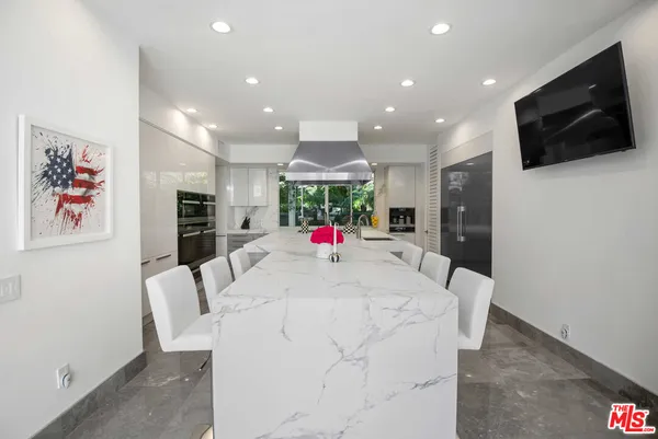 a large white kitchen with stainless steel appliances wooden floor and a flat screen tv
