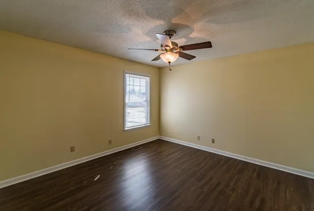 an empty room with wooden floor fan and windows