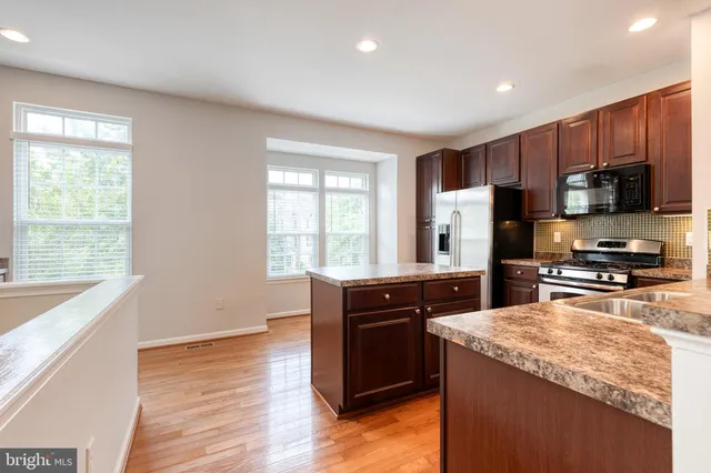 a kitchen with stainless steel appliances granite countertop a stove a sink dishwasher a refrigerator and a microwave oven with wooden floor