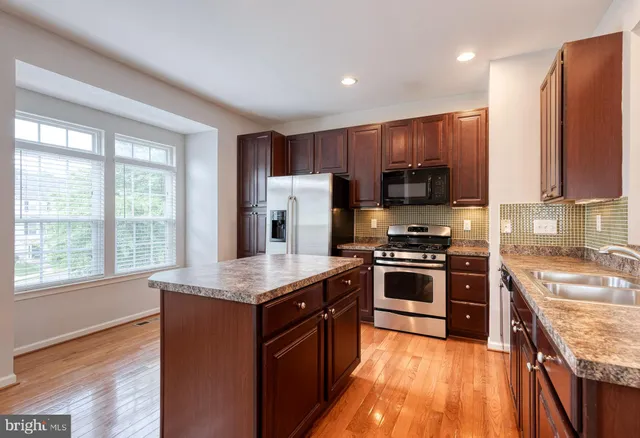 a kitchen with kitchen island granite countertop wooden floors stainless steel appliances a sink and a window