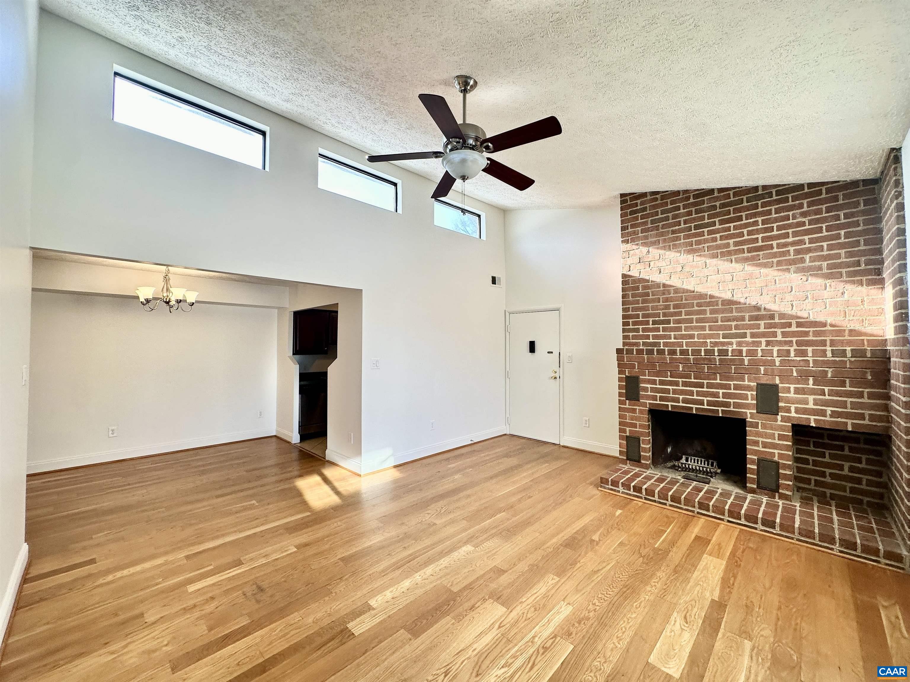 a view of an empty room with wooden floor fireplace and a window
