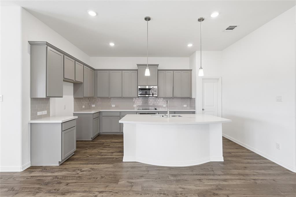 2529 Rivers W Road Anna, TX 75409 - Photo 13 of 40 Modern kitchen featuring a large central island, light gray cabinetry, stainless steel appliances, a tile backsplash, and wood-finish flooring