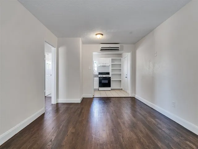 a view of empty room with wooden floor and kitchen