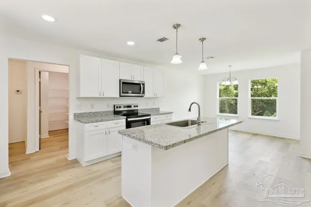 a kitchen with granite countertop a sink white cabinets and stainless steel appliances